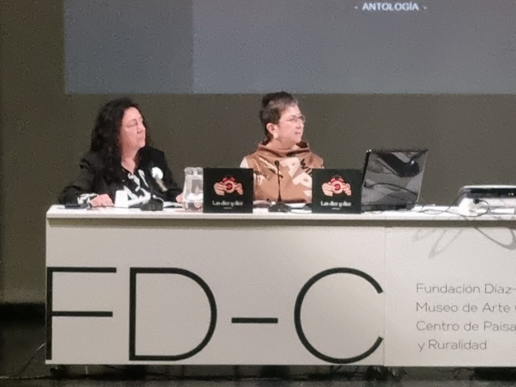 Plano cerrado de la mesa presidencial del acto. Dos mujeres coordinadoras con ejemplares del libro Las diez y diez. Logo de la Fundación Díaz-Caneja al frente.