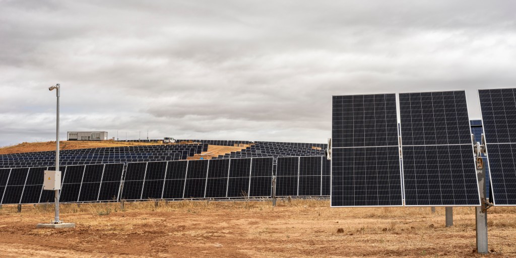 Vista panorámica de instalación de paneles solares fotovoltaicos sobre terreno árido, con filas de módulos orientables en estructura metálica y cielo cubierto.