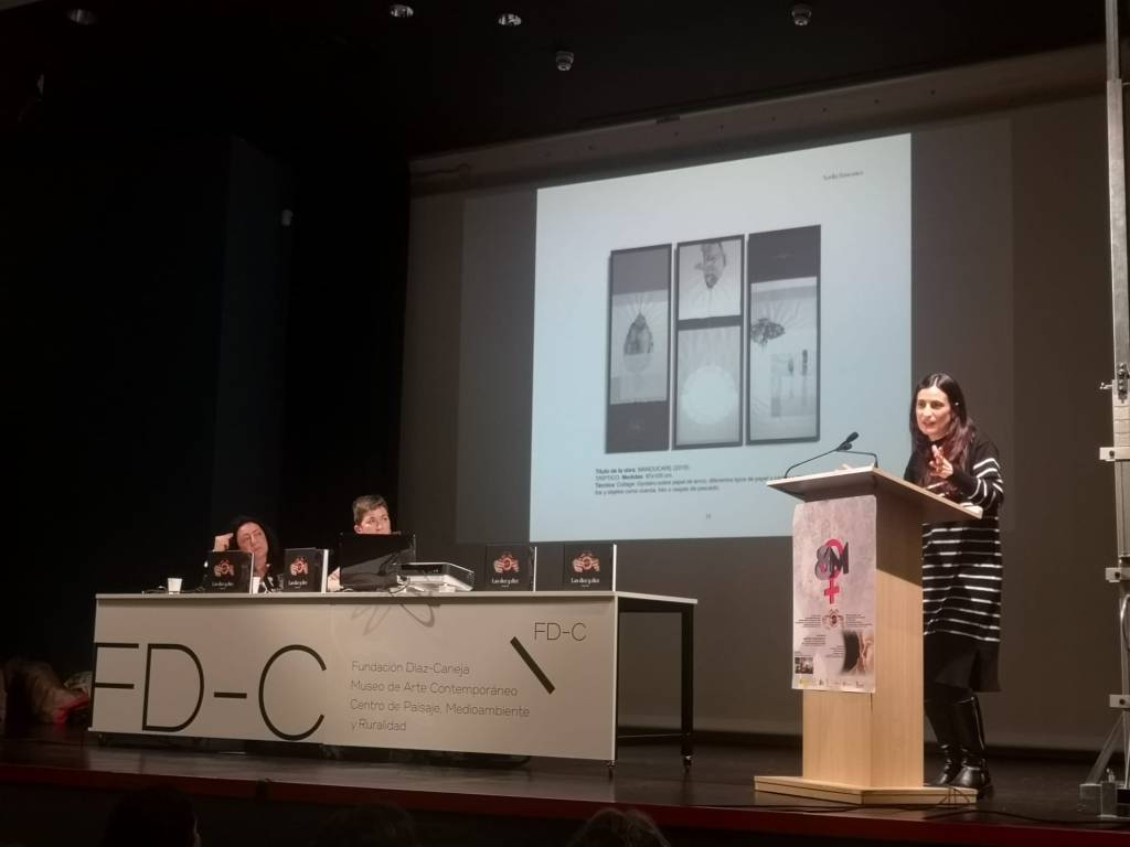 Acto de presentación en la Fundación Díaz-Caneja. Mesa presidencial con dos coordinadoras. En la pantalla, tríptico MANOUCARE de Noelia Báscones: collage sobre papel de arroz.