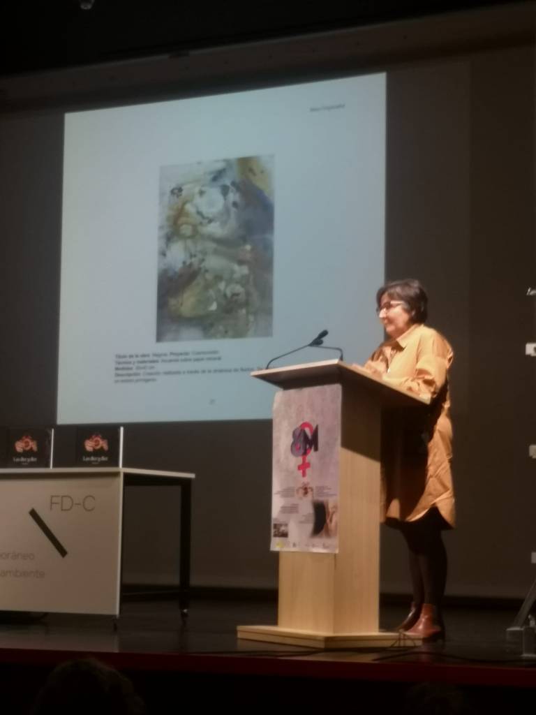 Presentación del libro en la Fundación Díaz-Caneja. Una artista habla en el atril. En la pantalla, imagen de textura abstracta en tonos tierra.